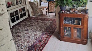 Un salon chaleureux avec un grand tapis, une bibliothèque, un fauteuil à motifs floraux et un meuble en bois aux portes vitrées.