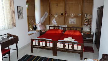Un dormitorio con cama de madera, una mesita de noche, una silla, un ventanal con cortinas y un estante en la pared con objetos decorativos.