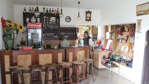 Zona de bar con taburetes de madera, un refrigerador y estantes con botellas y vasos.