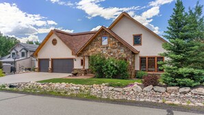 A two-story house with a stone facade, a large garage, and a well-maintained front yard with a rock garden and trees. - Cherry Drive 4 Bedroom Home by RedAwning (Steamboat Springs)