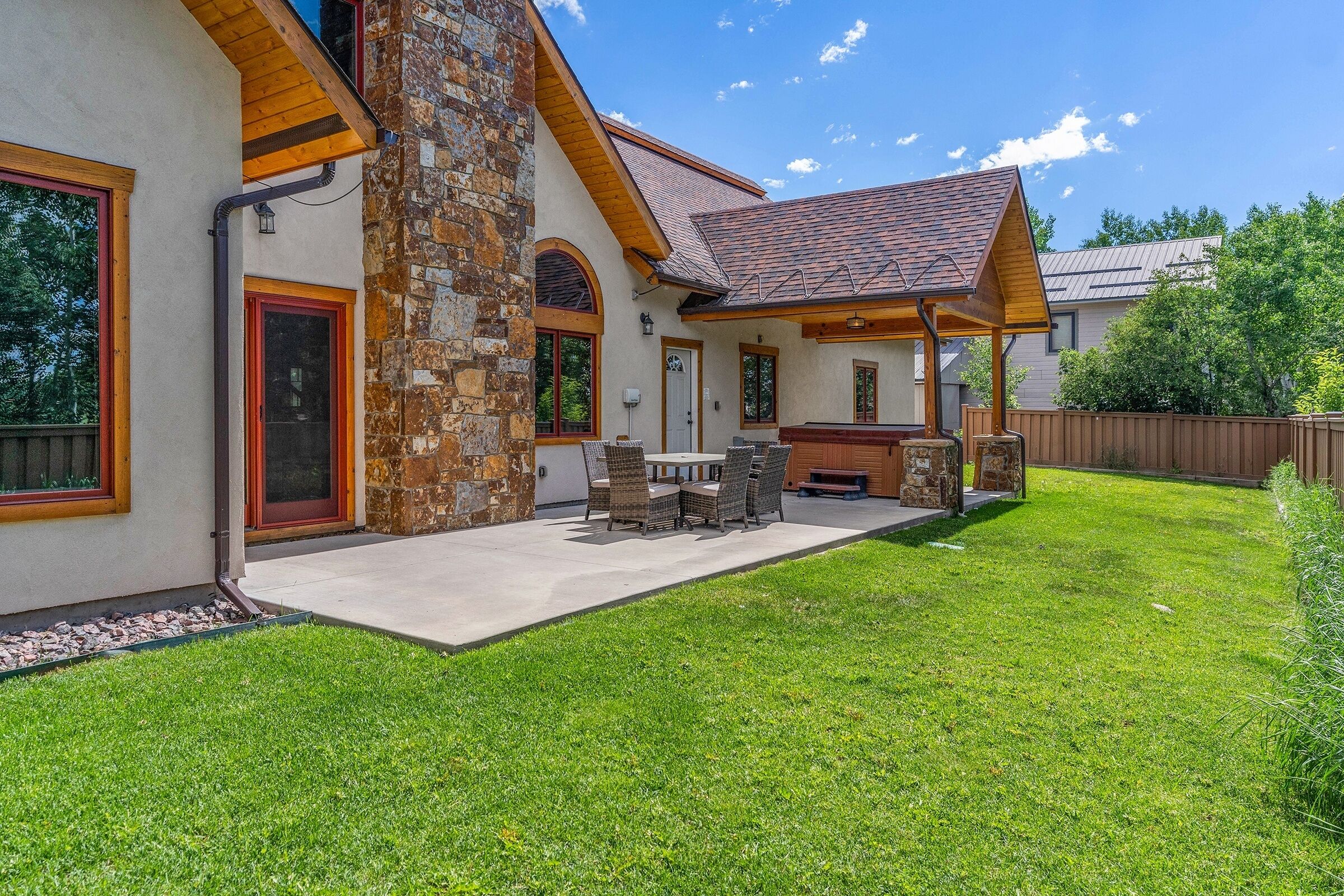 Une maison avec une façade en pierre, un patio couvert avec une table et des chaises, et une pelouse bien entretenue.