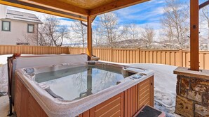 A hot tub under a wooden pergola with a stone wall and a view of a house and trees. - Cherry Drive 4 Bedroom Home by RedAwning (Steamboat Springs)