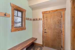 A wooden bench, a window with a view of a snowy landscape, and a wooden door with a coat rack above it.