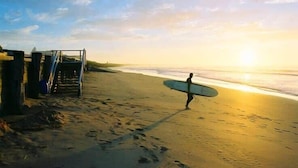 A beach scene with a person carrying a surfboard, a staircase, and a clear sky. - Sunny Daze Haven: SPA and Pool (Ocean Grove)
