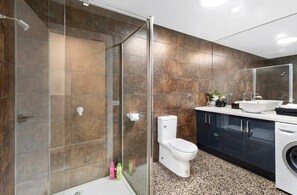 Een moderne badkamer met een douchecabine van glas, een toilet, een wastafel en een wasmachine.