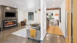 A modern living room with a fireplace, a sofa, and a dining area. - Sunny Daze Haven: SPA and Pool (Ocean Grove)