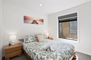 Un dormitorio con cama, mesitas de noche, una ventana con vistas y un cuadro en la pared.