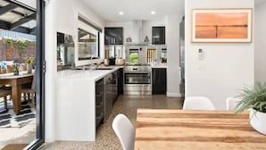 A modern kitchen with stainless steel appliances, a wooden dining table, and a large window. - Sunny Daze Haven: SPA and Pool (Ocean Grove)