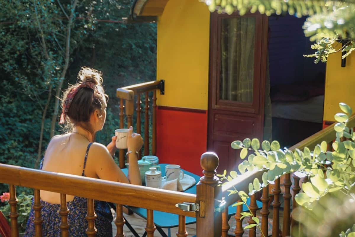 A woman sitting at a table on a wooden deck with a small building in the background.