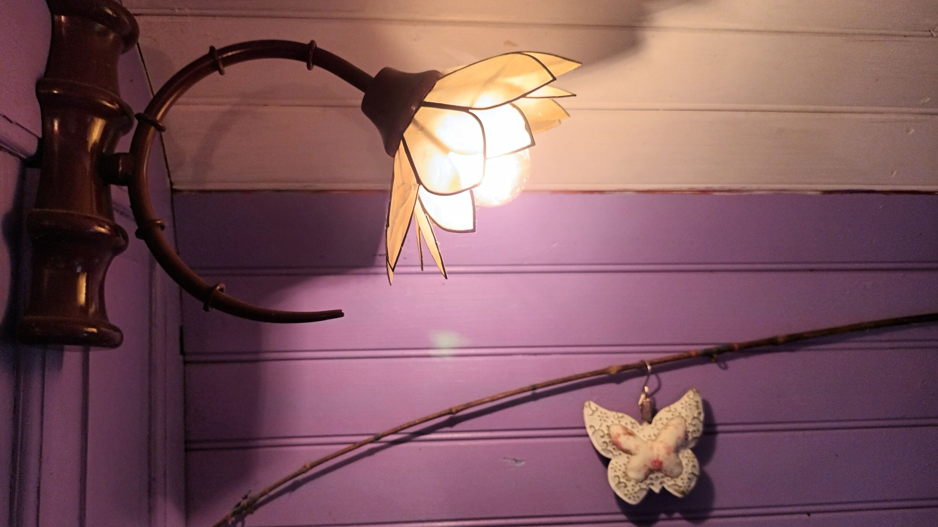 Een wandlamp met een gebogen arm en een bloemvormige lampenkap.