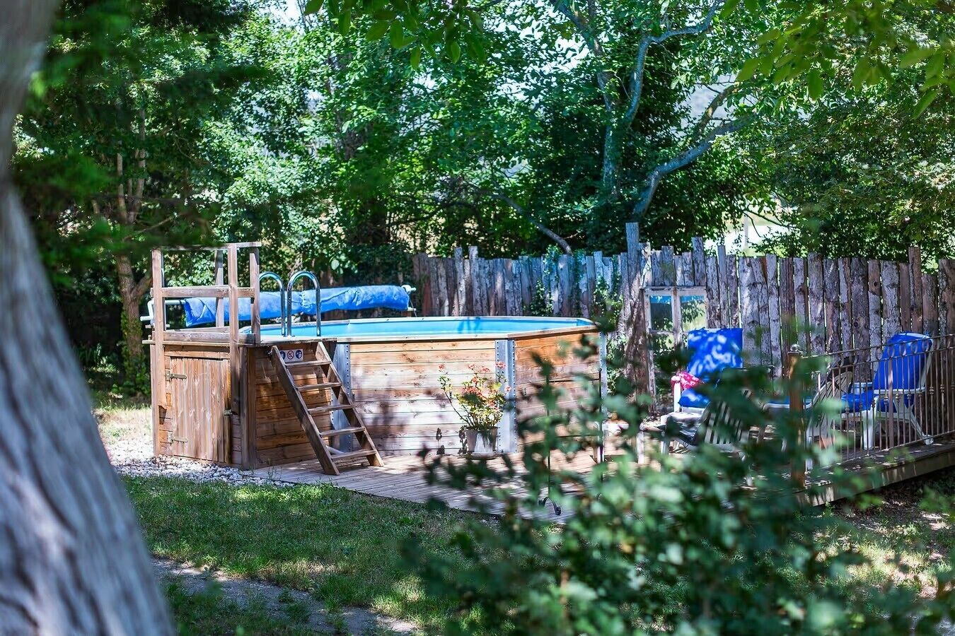 A backyard with a wooden deck, a small pool, and a fenced area with blue chairs.