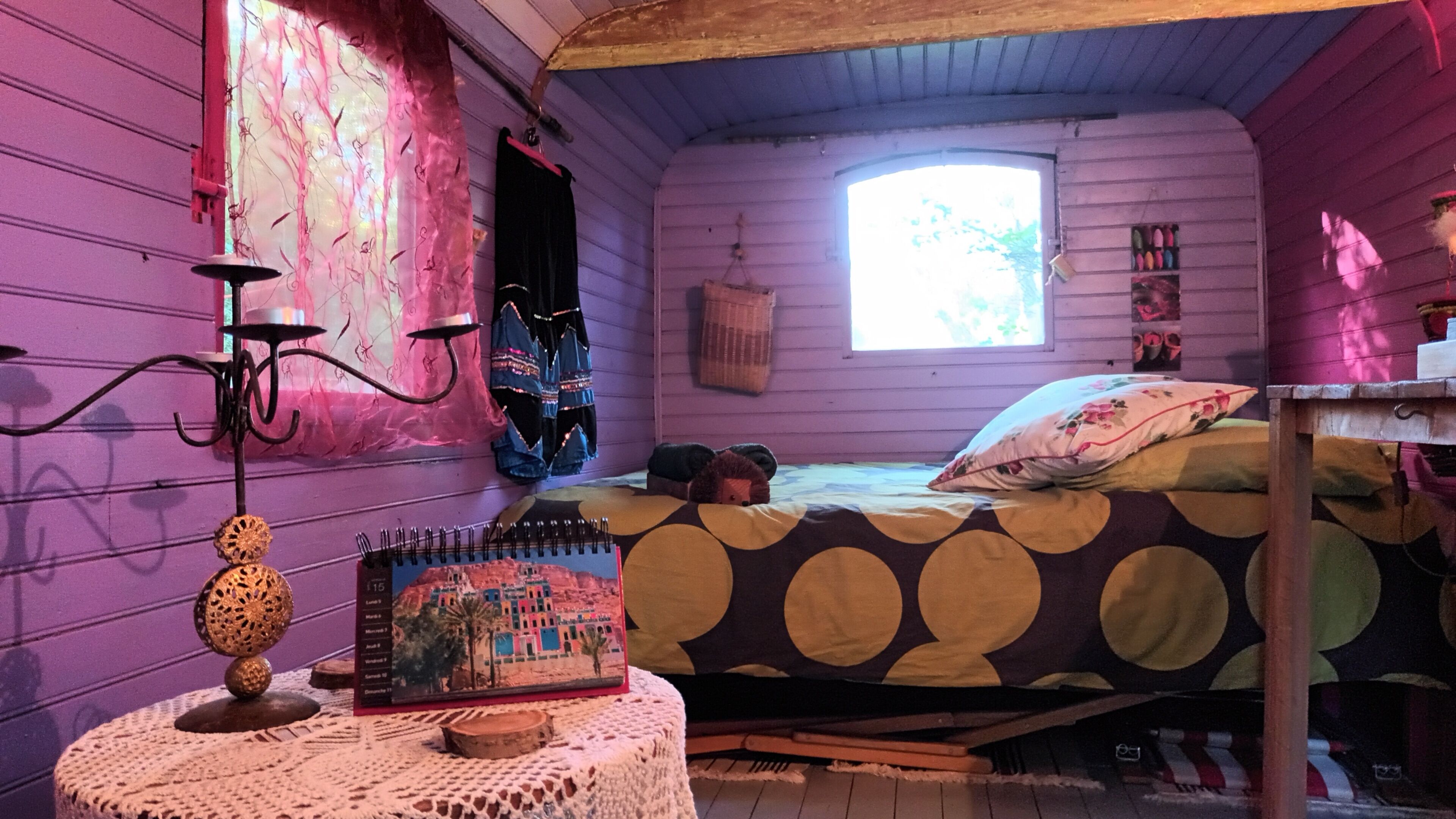 Una cabaña acogedora con una cama, una mesita con un libro y una ventana.