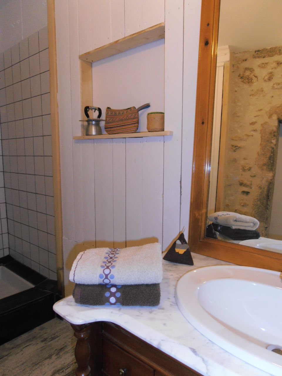 Casa de banho com lavatório branco, espelho, toalha e prateleira com artigos de higiene pessoal.