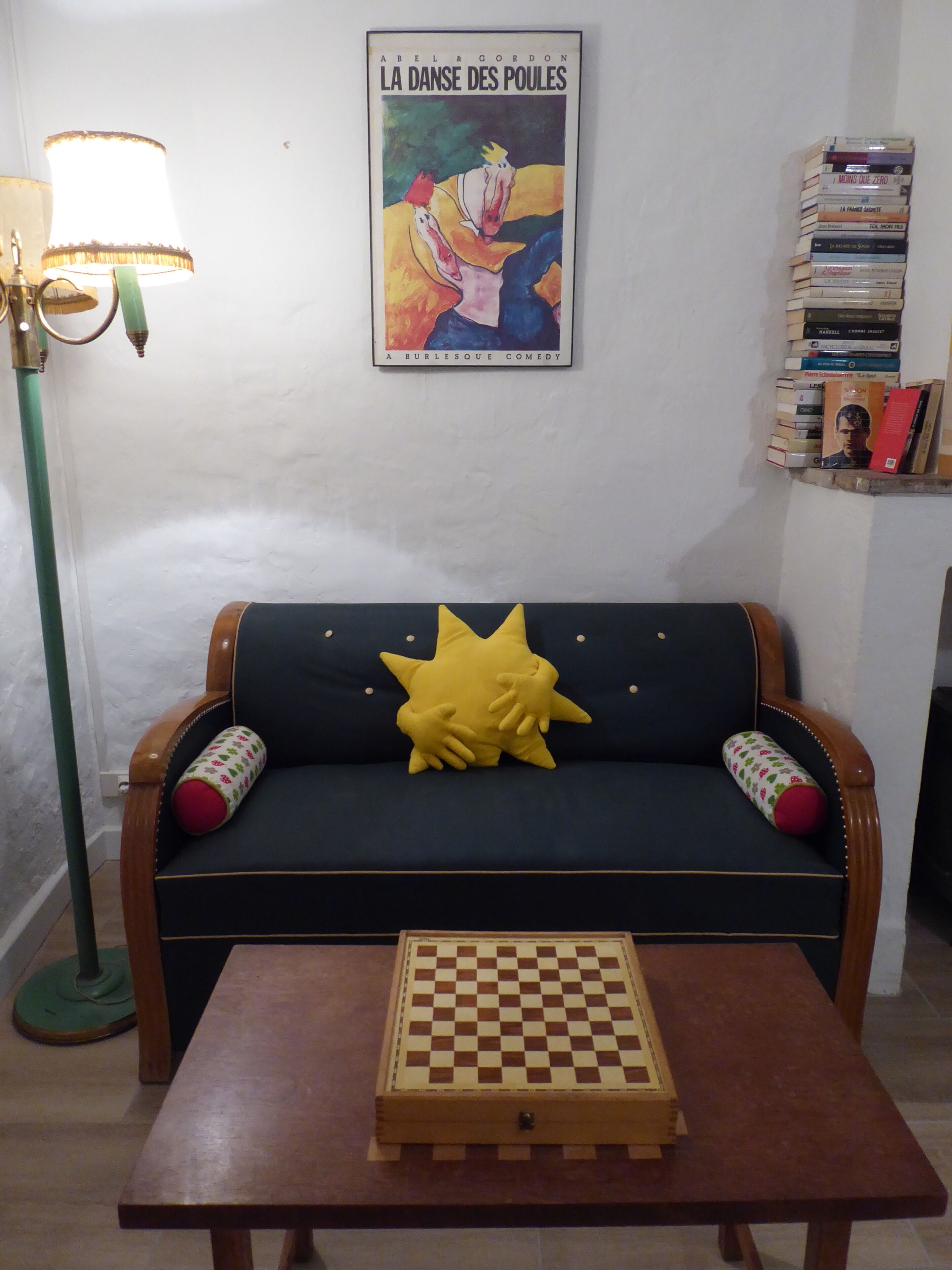 A living room with a sofa, a lamp, a poster, and a chessboard.