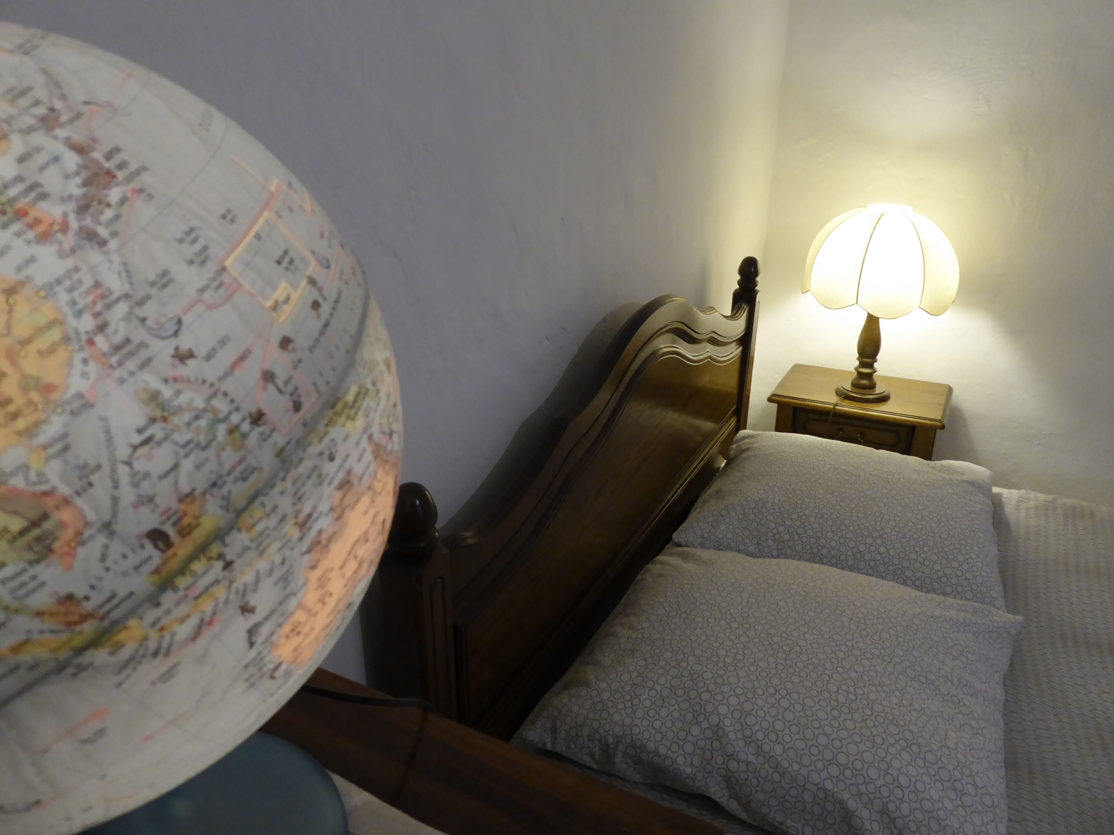 A bed with a wooden headboard, a globe, and a bedside table with a lamp.