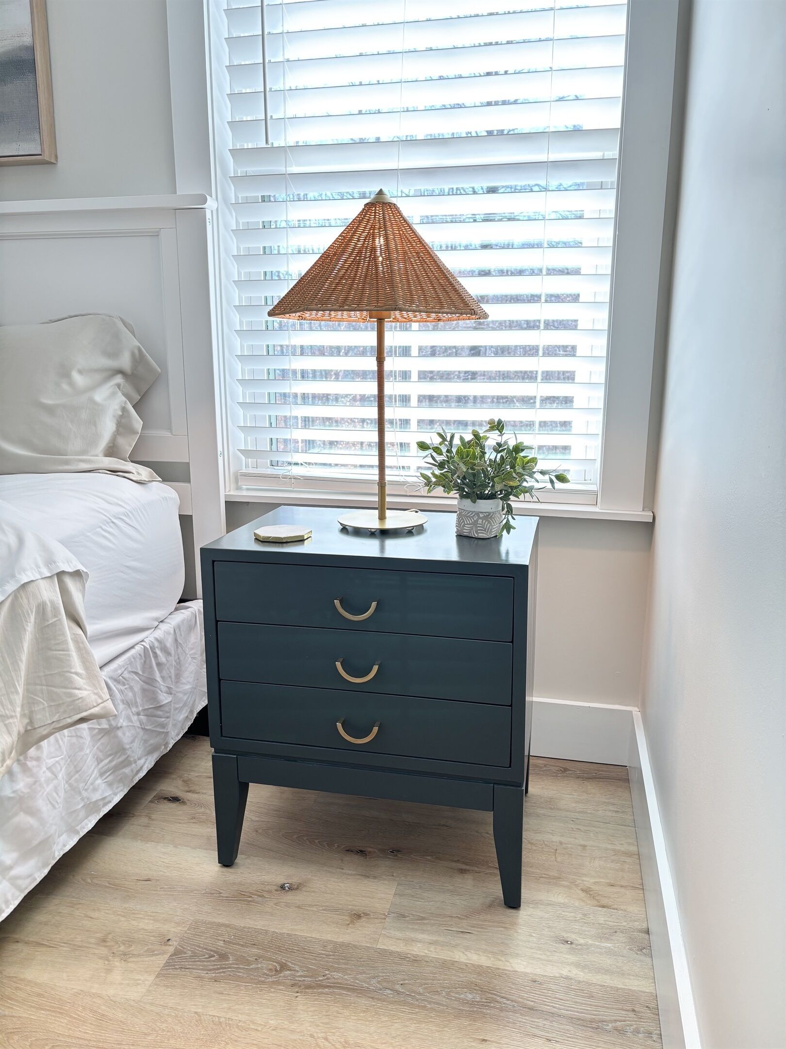 Une chambre à coucher avec un lit, une table de chevet avec une lampe et une fenêtre avec des stores.