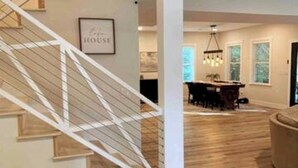 A staircase with a white railing leading to a dining area with a chandelier and a table. - Lake Access ~ King Ensuites w/ fireplaces~ Hot Tub~ Fire Pit~ Boat Ramp (Monticello)