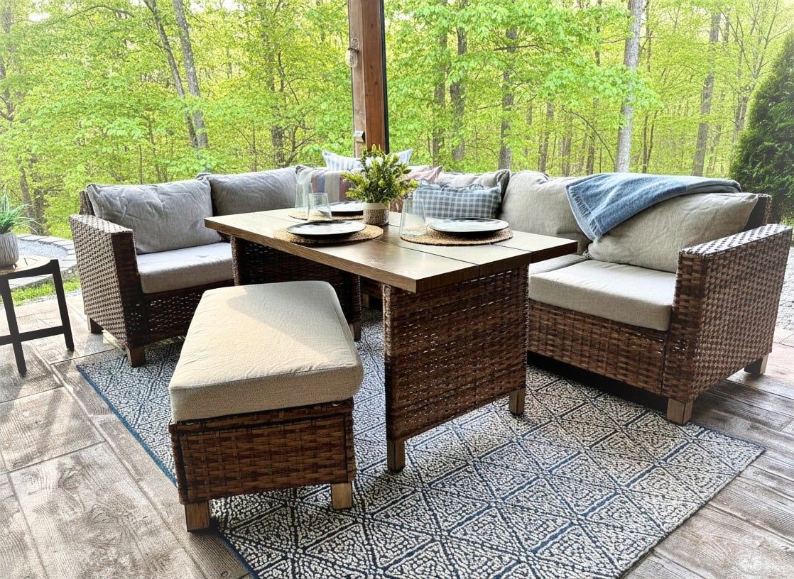 An outdoor patio with wicker furniture, a table, and a view of a forest.