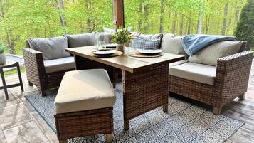 An outdoor patio with wicker furniture, a table, and a view of a forest.