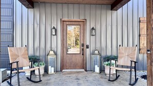 A wooden porch with two rocking chairs, a wooden door, and two wall-mounted lanterns. - Lake Access ~ King Ensuites w/ fireplaces~ Hot Tub~ Fire Pit~ Boat Ramp (Monticello)