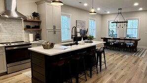 A modern kitchen with a central island, wooden flooring, and pendant lighting. - Lake Access ~ King Ensuites w/ fireplaces~ Hot Tub~ Fire Pit~ Boat Ramp (Monticello)