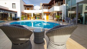 Una piscina rodeada de sillas de mimbre y un edificio con tejado de baldosas.