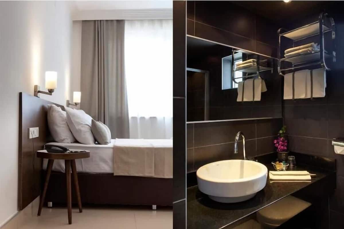 A modern hotel room with a bed, bedside table, and a bathroom with a sink and towel rack.