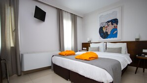 Habitación de hotel con cama, mesita de noche, silla, televisor montado en la pared y ventana con cortinas.