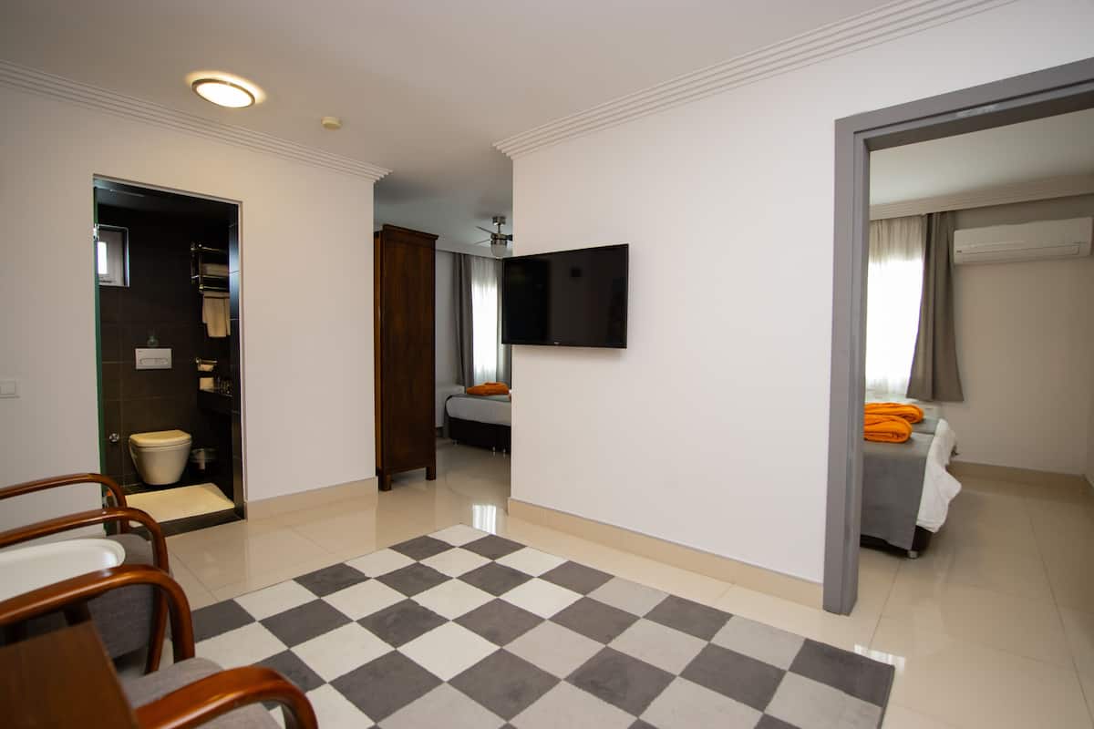 A hotel room with a checkered floor, a flat-screen TV mounted on the wall, a bed with an orange blanket, and a bathroom visible through an open door.