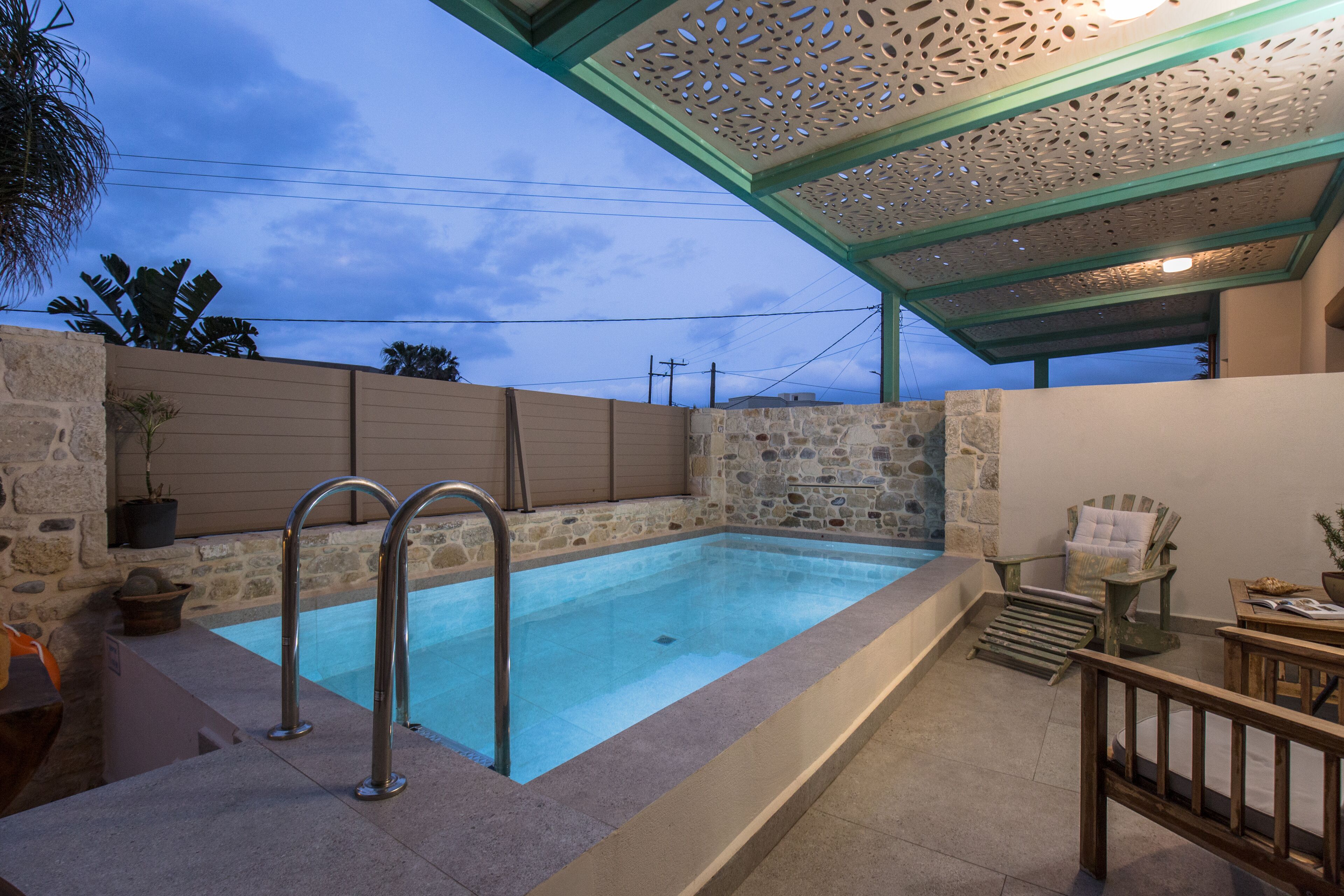 Una piscina con paredes de piedra, una escalera metálica y un muelle de madera con una silla y una mesa.