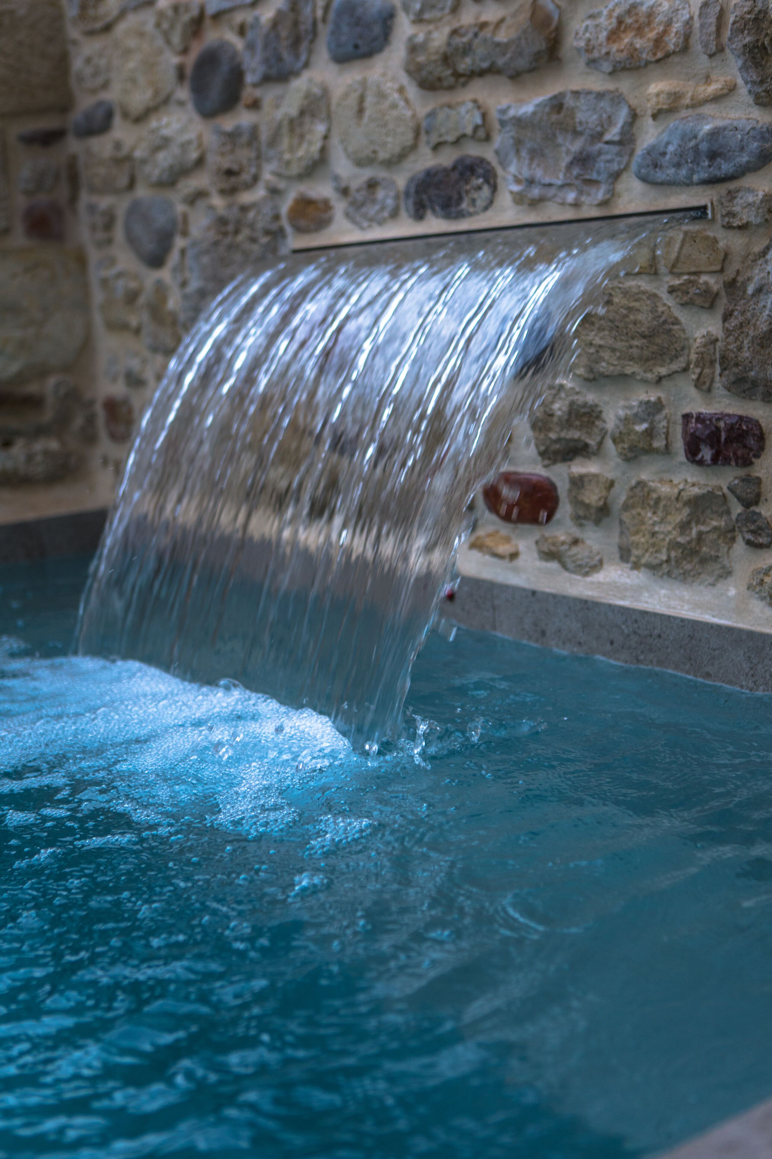 A stone wall with a waterfall feature in a pool.