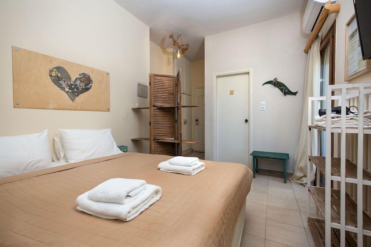 A bedroom with a bed, a wooden bench, a wall-mounted shelf, and a door.