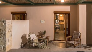 Un área de piscina con sillas y una mesa de madera, un muro de piedra y vistas a una cocina.