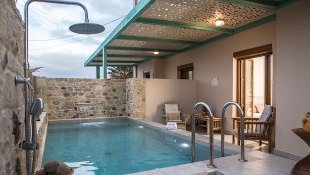 Una piscina techada con paredes de piedra, una ducha, un área de descanso pequeña y vistas al exterior.