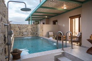 A stone-walled indoor swimming pool with a shower, a small seating area, and a view of the outdoors. - Arodamos Apartments & Studios (Kissamos)