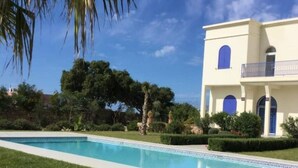 A poolside view of a two-story building with a balcony, surrounded by greenery and a clear sky. - Riyad Azul between nature and the ocean (Sidi Kaouki)