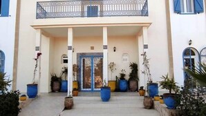 A building with a covered entrance, large potted plants, and a balcony with a railing. - Riyad Azul between nature and the ocean (Sidi Kaouki)