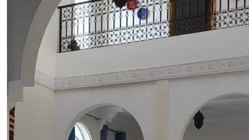Ein großzügiger Innenraum mit hoher Decke, ein Balkon mit dekorativer Geländer und eine Essecke mit Tisch und Stühlen.