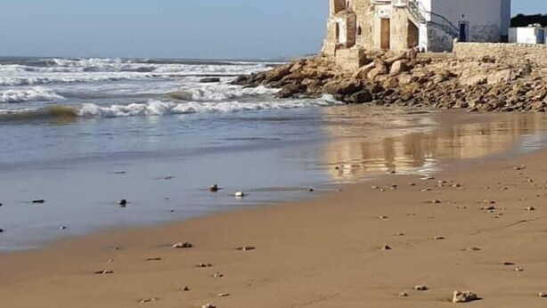 A coastal building with a stone base and white upper structure, situated on a sandy beach with scattered rocks. - Riyad Azul between nature and the ocean (Sidi Kaouki)