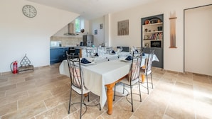 A dining area with a table set for four, a kitchen in the background, and a bookshelf with various items.
