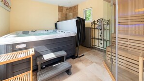 A modern bathroom with a hot tub, wooden benches, a glass shower enclosure, and a statue.