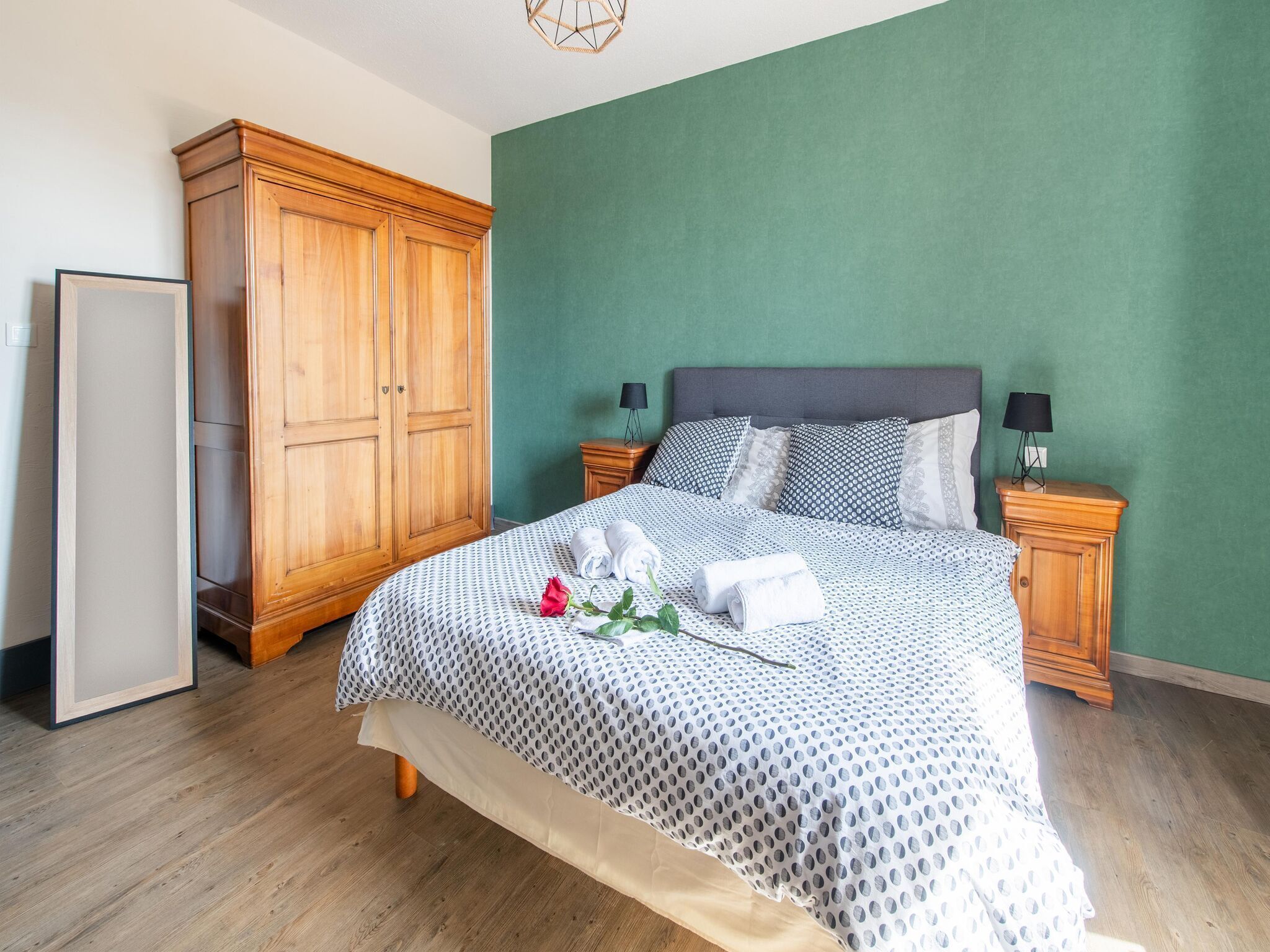 Un dormitorio con cama, armario de madera, paredes verdes y suelo de madera.