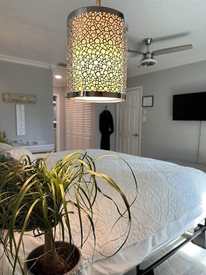 A bedroom with a bed, a ceiling fan, a wall-mounted TV, and a potted plant.