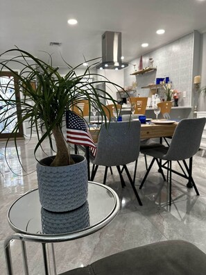 Un comedor moderno con una mesa de vidrio, sillas y una planta en maceta con una bandera estadounidense.