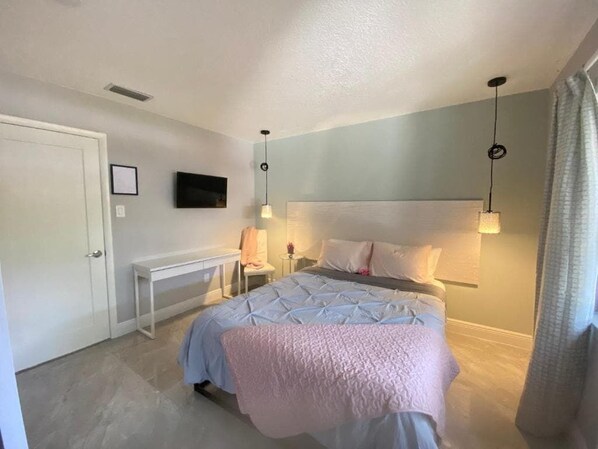 Un dormitorio con cama, mesitas de noche, televisión y cabecero.
