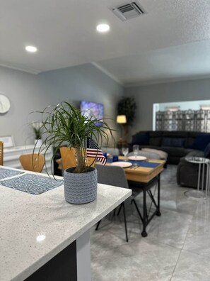 Ett modernt vardagsrum med en matplats, med en krukväxt prydd med en amerikansk flagga, en tv och utsikt över stadens skyline.