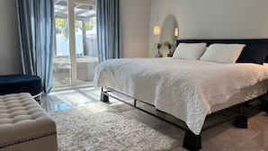 A bedroom with a bed, a bedside table, a chair, a large window with curtains, and a view of the outdoors. - Florida Vacation Villa with hot tub (Fort Lauderdale)