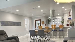 A modern living room with a dining area, a kitchen, and a large window. - Florida Vacation Villa with hot tub (Fort Lauderdale)