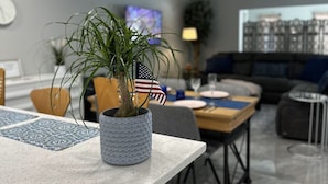 A modern living room with a dining area, featuring a potted plant with an American flag, a television, and a cityscape view through the window. - Florida Vacation Villa with hot tub (Fort Lauderdale)
