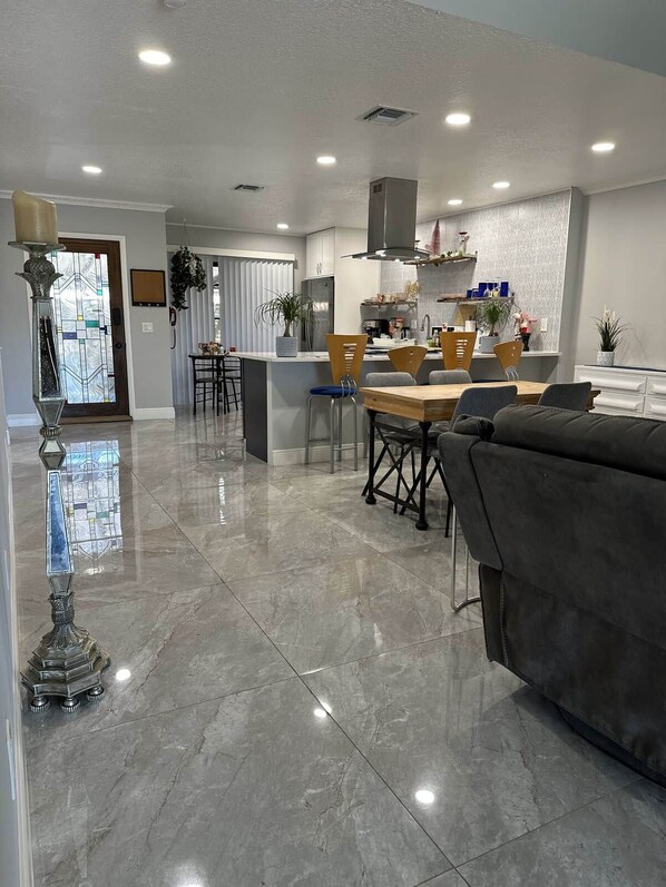 A modern kitchen with a central island, a dining area with a wooden table and chairs, and a living area with a sofa and a decorative floor lamp.